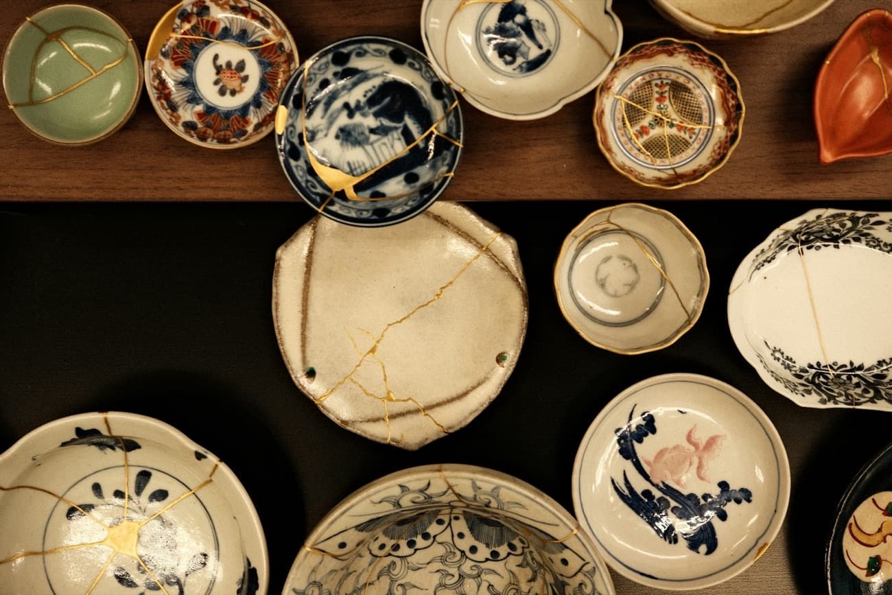 Una raccolta di piatti e ciotole di ceramica giapponese, molti riparati con l'oro del kintsugi, disposti su un tavolo scuro