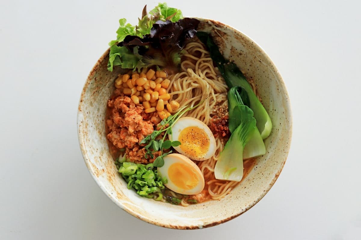 Una ciotola di ramen vista dall'alto, con uovo, verdure e mais