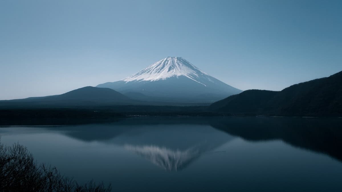 Il Monte Fuji innevato che si specchia in un lago calmo all'alba, con i monti scuri intorno