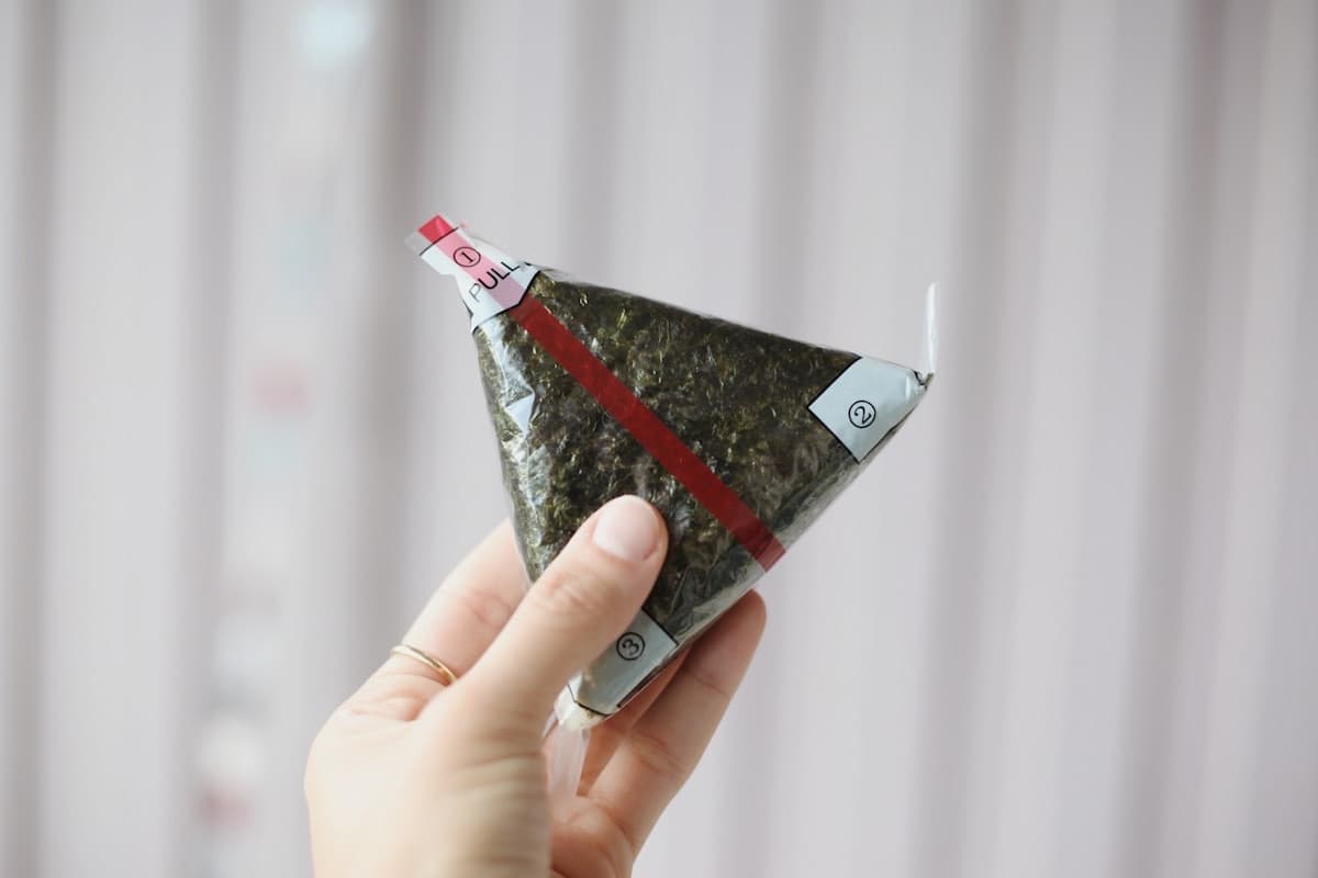Una mano tiene un onigiri confezionato, con le linguette numerate per aprirlo
