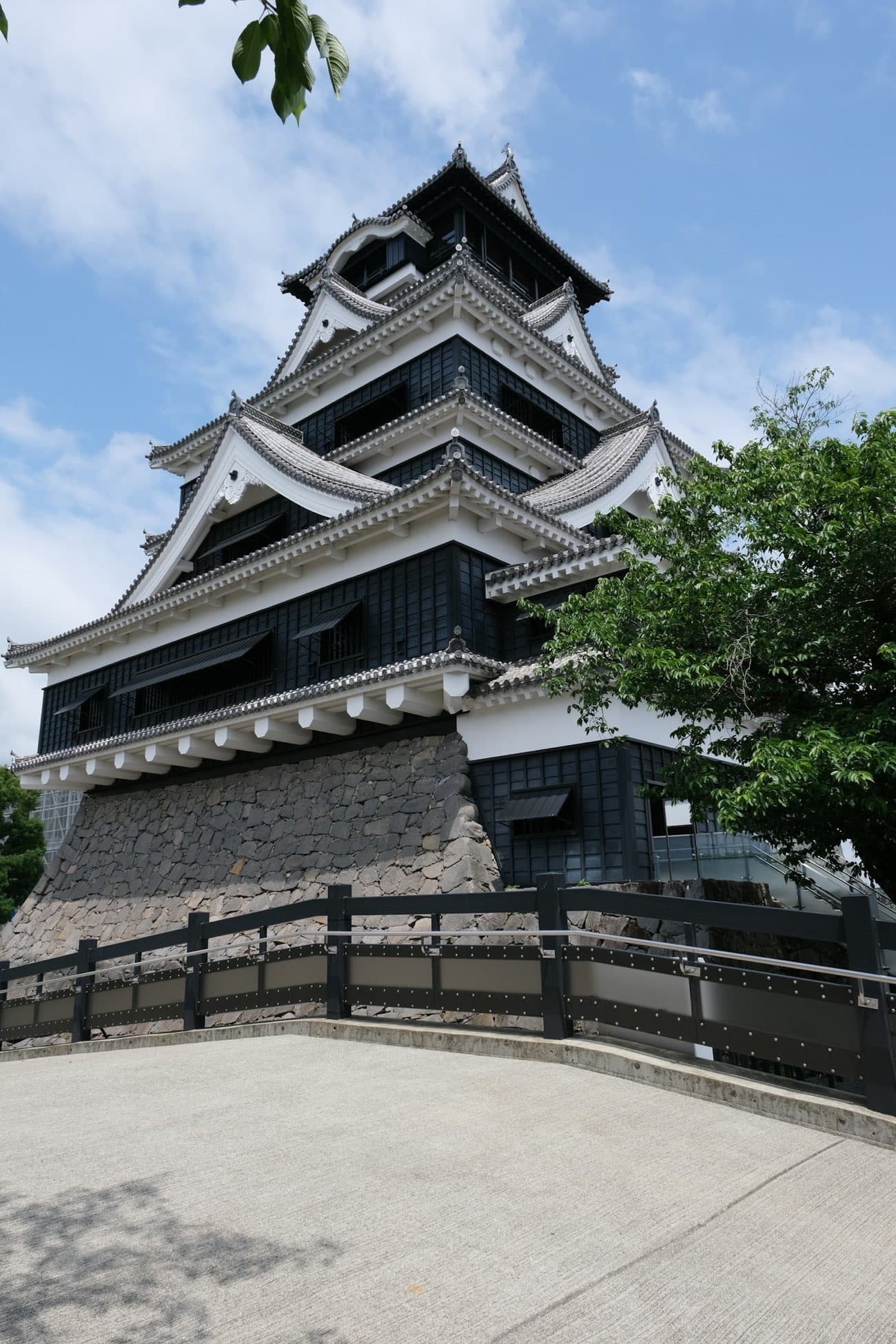 Il castello di Kumamoto, grande donjon nero e bianco su un'imponente base di pietra, sotto un cielo azzurro