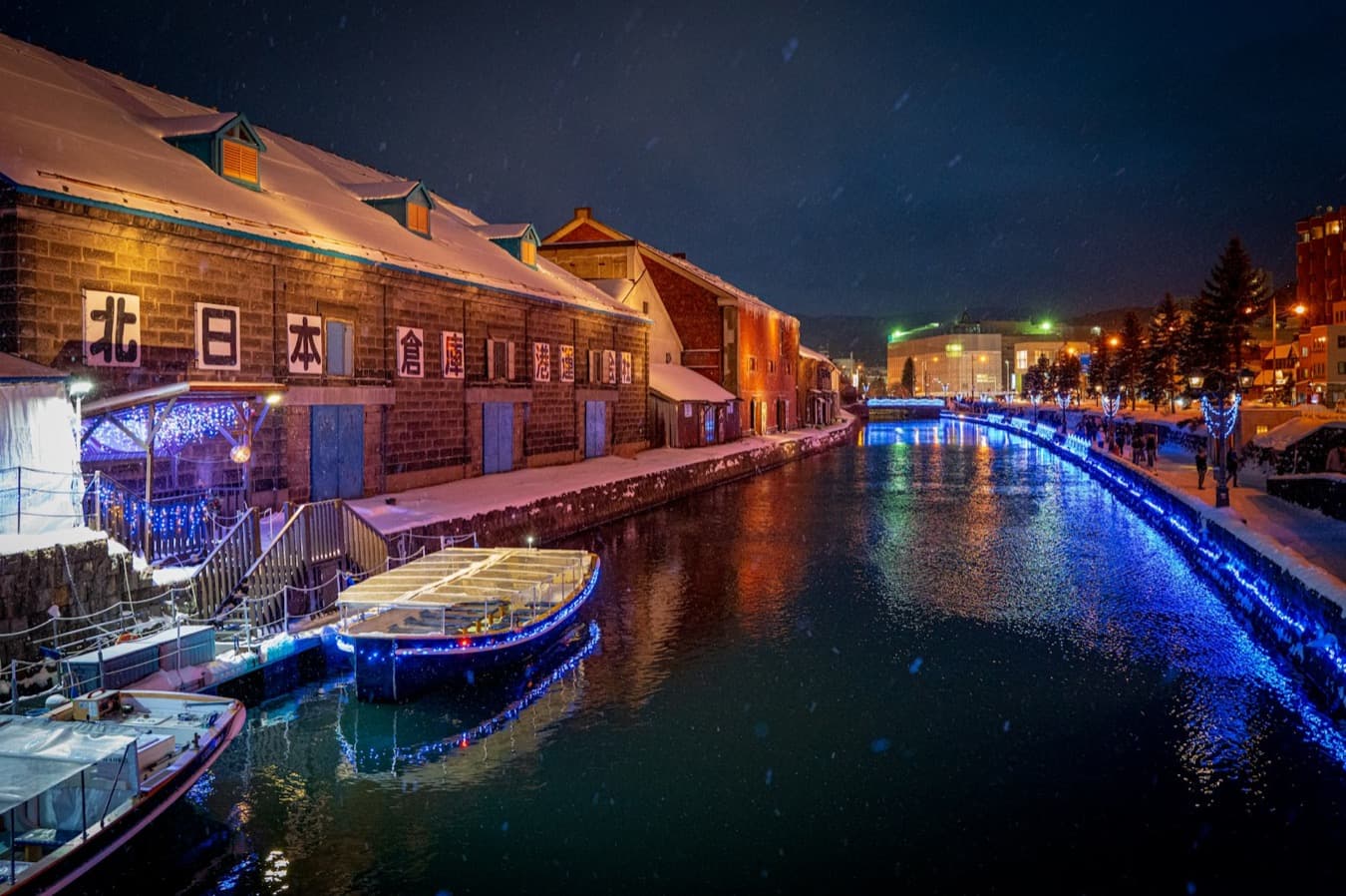 Il canale di Otaru sotto la neve di notte, con i magazzini di pietra illuminati e i lampioni a gas