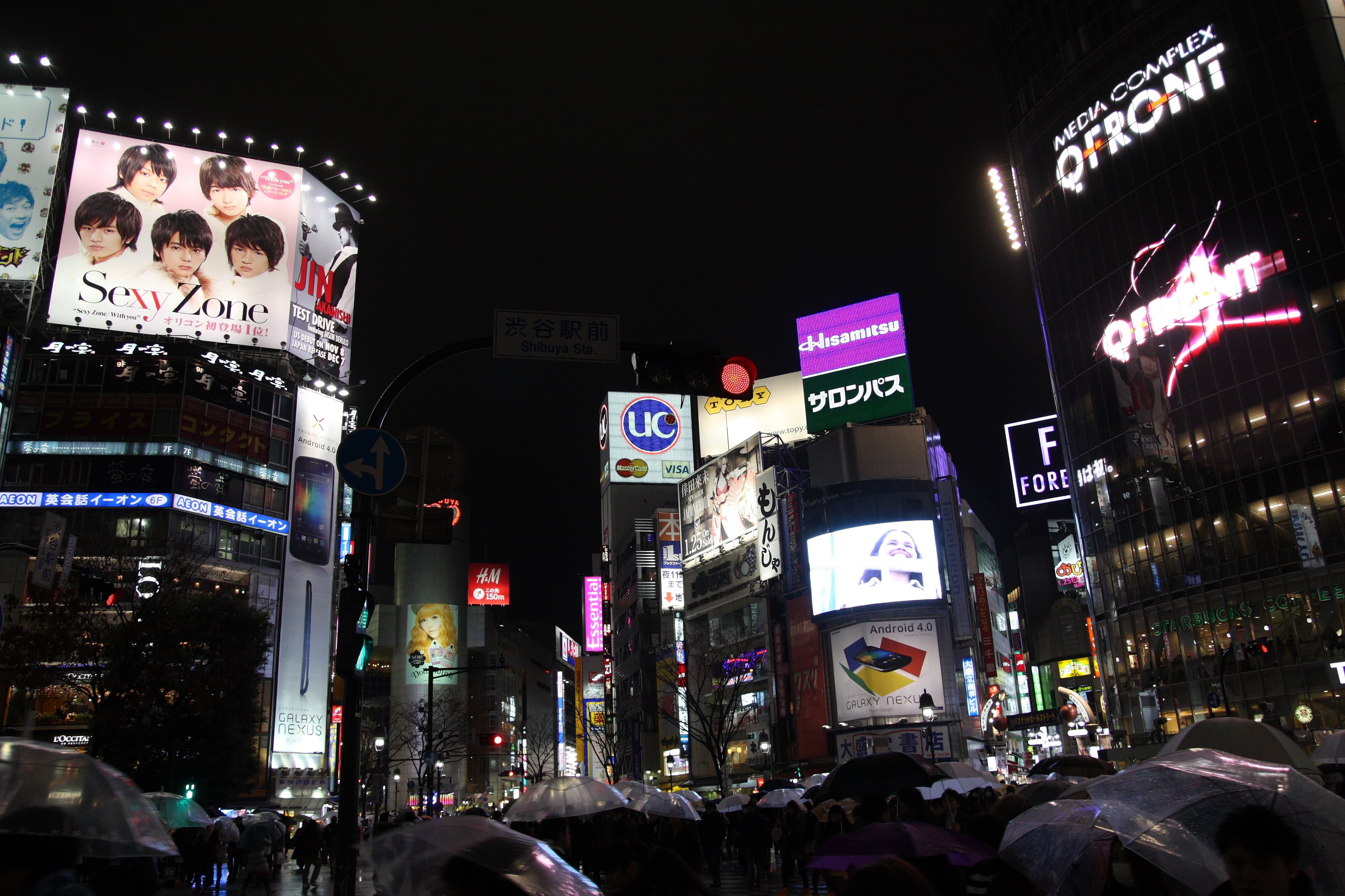 L'incrocio di Shibuya a Tokyo di notte, con i neon e i grandi schermi illuminati — il quartiere ha anche una vivace scena gastronomica