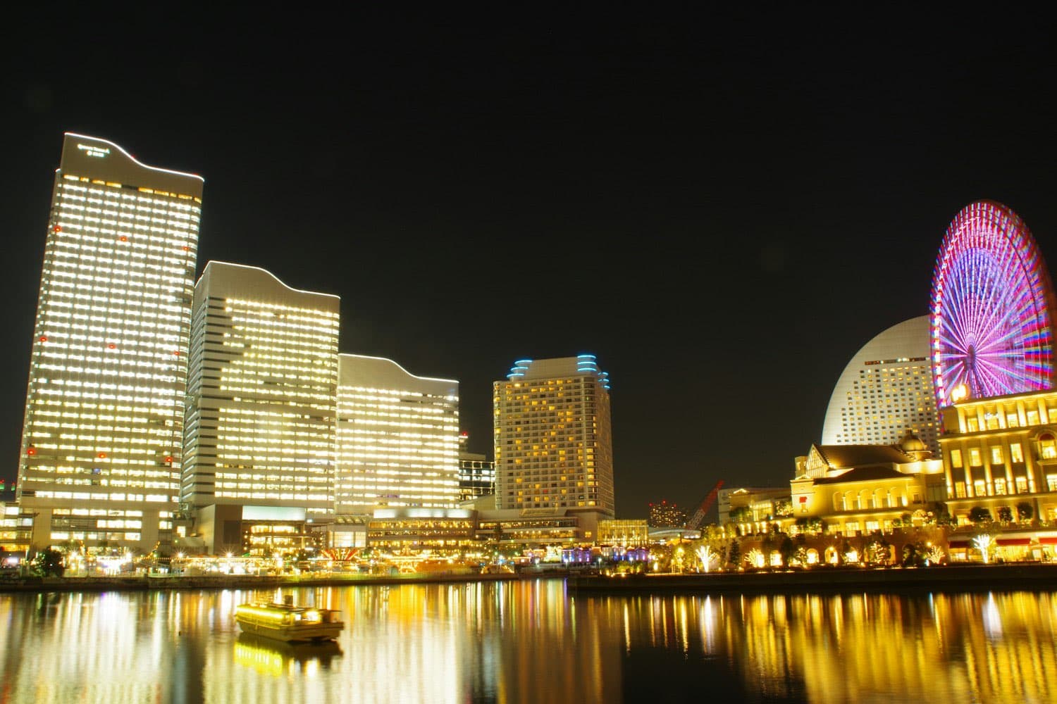 Il panorama notturno di Minato Mirai a Yokohama: grattacieli illuminati d'oro, la ruota panoramica colorata e i riflessi sull'acqua del porto