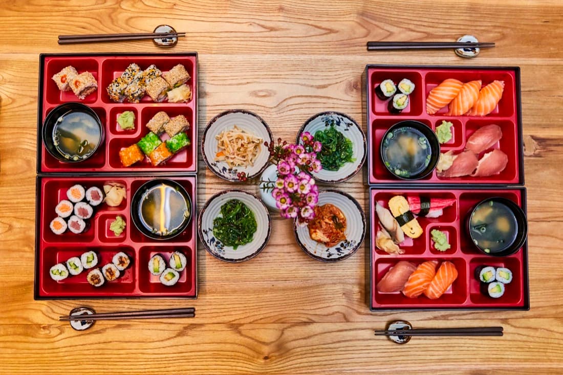Quattro bento in scatole di lacca rossa viste dall'alto, con sushi, riso e contorni
