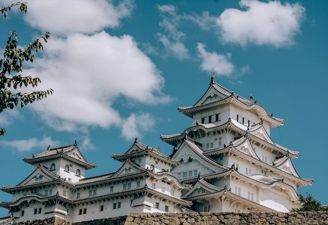 Il castello di Himeji, bianco e imponente, si erge contro un cielo azzurro sopra le sue mura di pietra