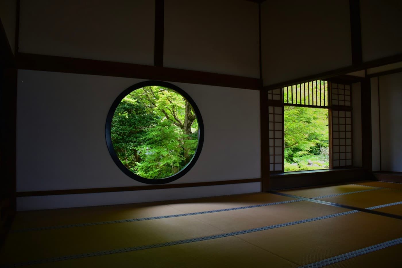 Una stanza di tatami con una grande finestra rotonda che inquadra il verde degli aceri del giardino