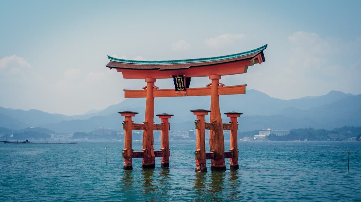 Il grande torii rosso di Miyajima che si erge sull'acqua, con le montagne sullo sfondo