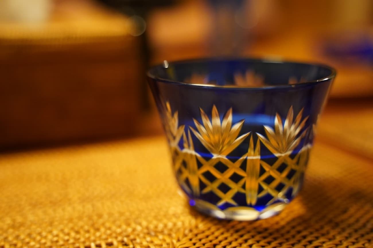Una piccola coppa da sake di cristallo Edo kiriko blu cobalto, incisa a mano con motivi geometrici finissimi, su una stuoia