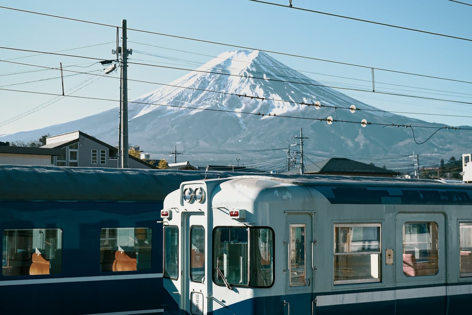 Il Monte Fuji innevato dietro un vecchio treno locale blu fermo in stazione, sotto un cielo azzurro