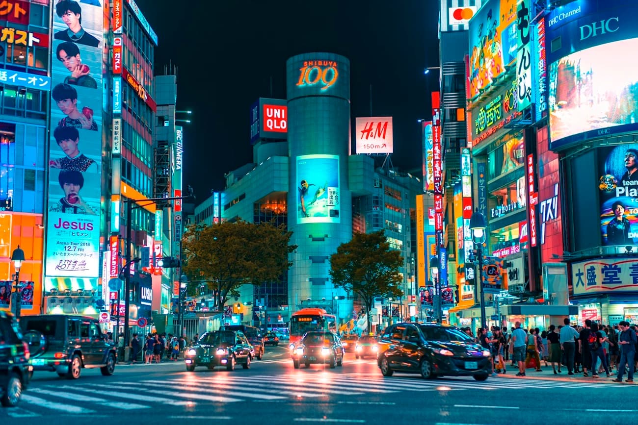 L'incrocio di Shibuya a Tokyo di notte, illuminato da mille insegne al neon, con le auto e la folla