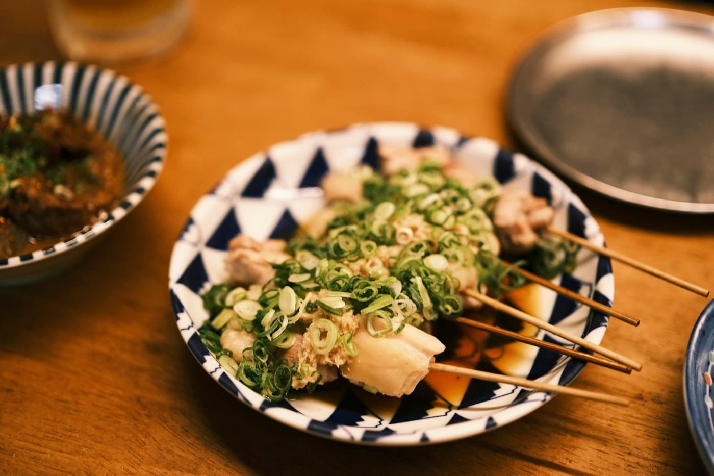 Spiedini di yakitori alla griglia su carbone, con la salsa tare lucida che caramella sul fuoco, in un'izakaya giapponese