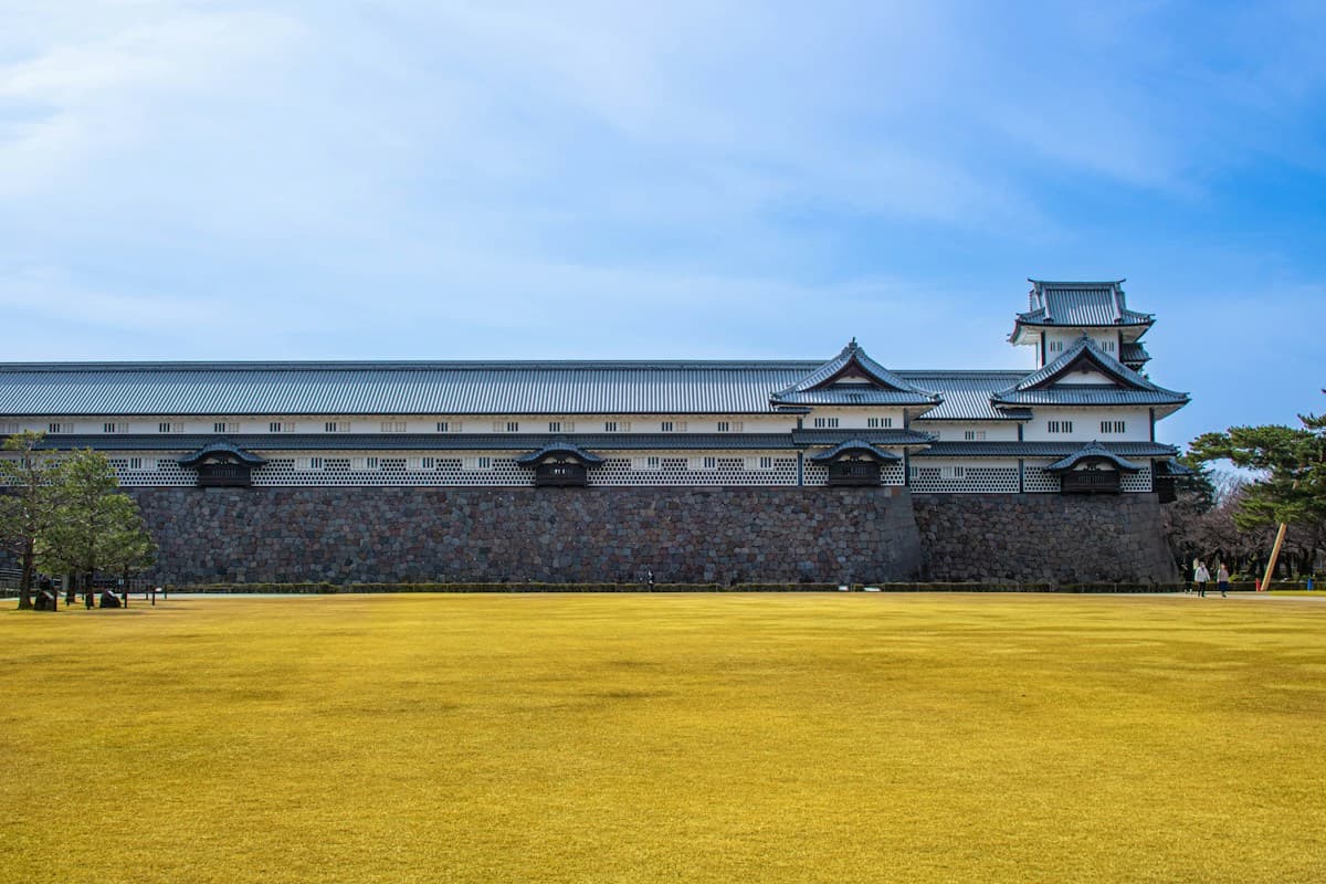 Il castello di Kanazawa con le sue mura bianche e le torri tradizionali, circondato da un vasto prato verde sotto un cielo azzurro