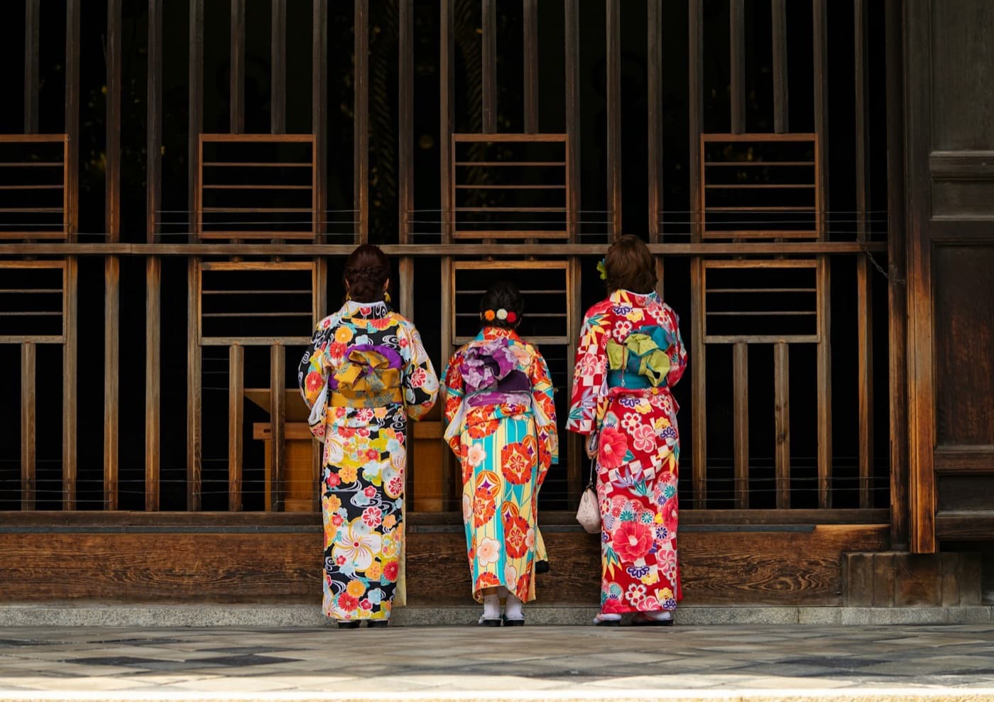 Tre ragazze in kimono colorati, viste di spalle, davanti a un santuario giapponese
