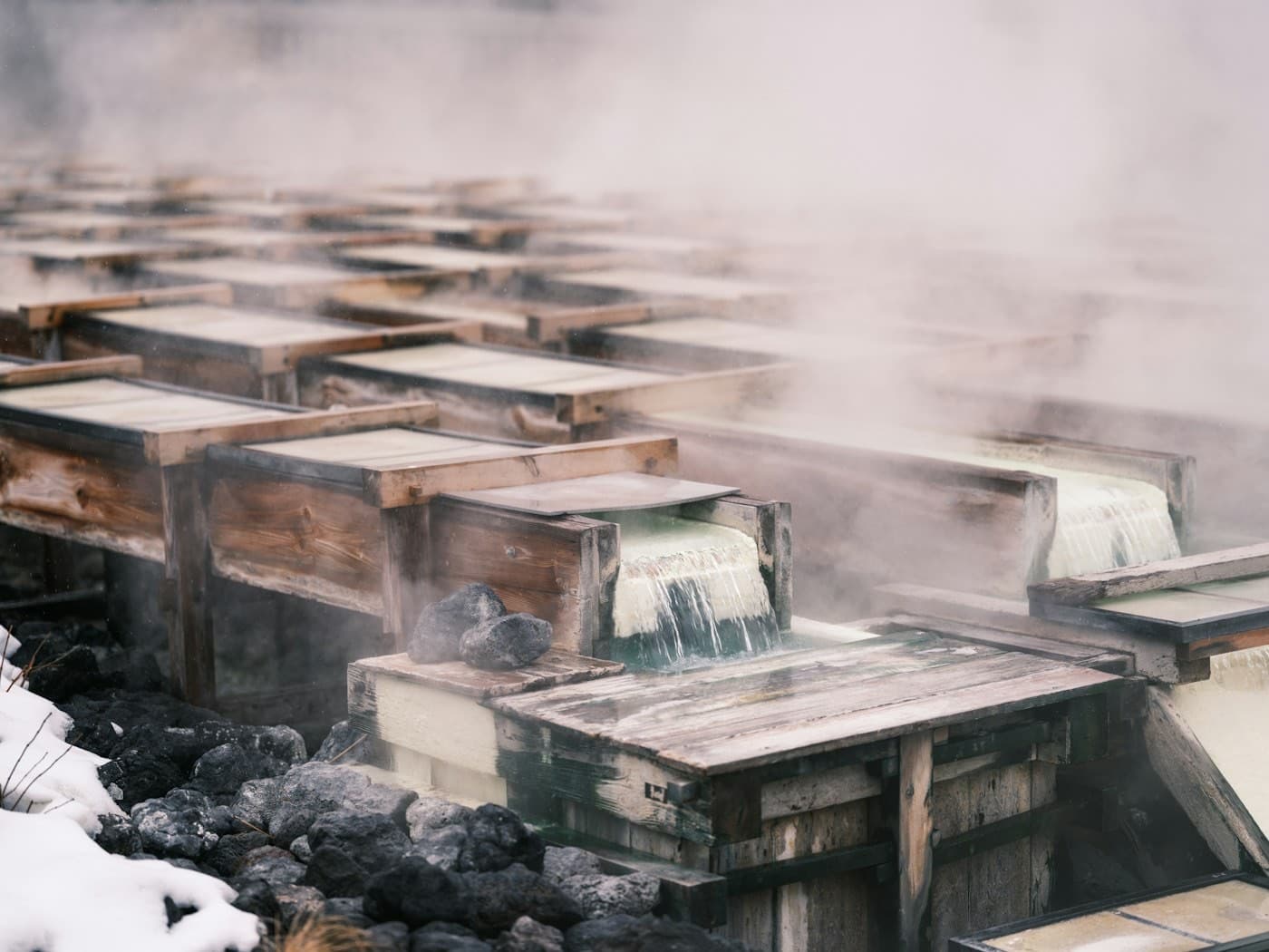 Lo Yubatake di Kusatsu: le canaline di legno da cui scorre l'acqua termale fumante, tra rocce vulcaniche coperte di neve