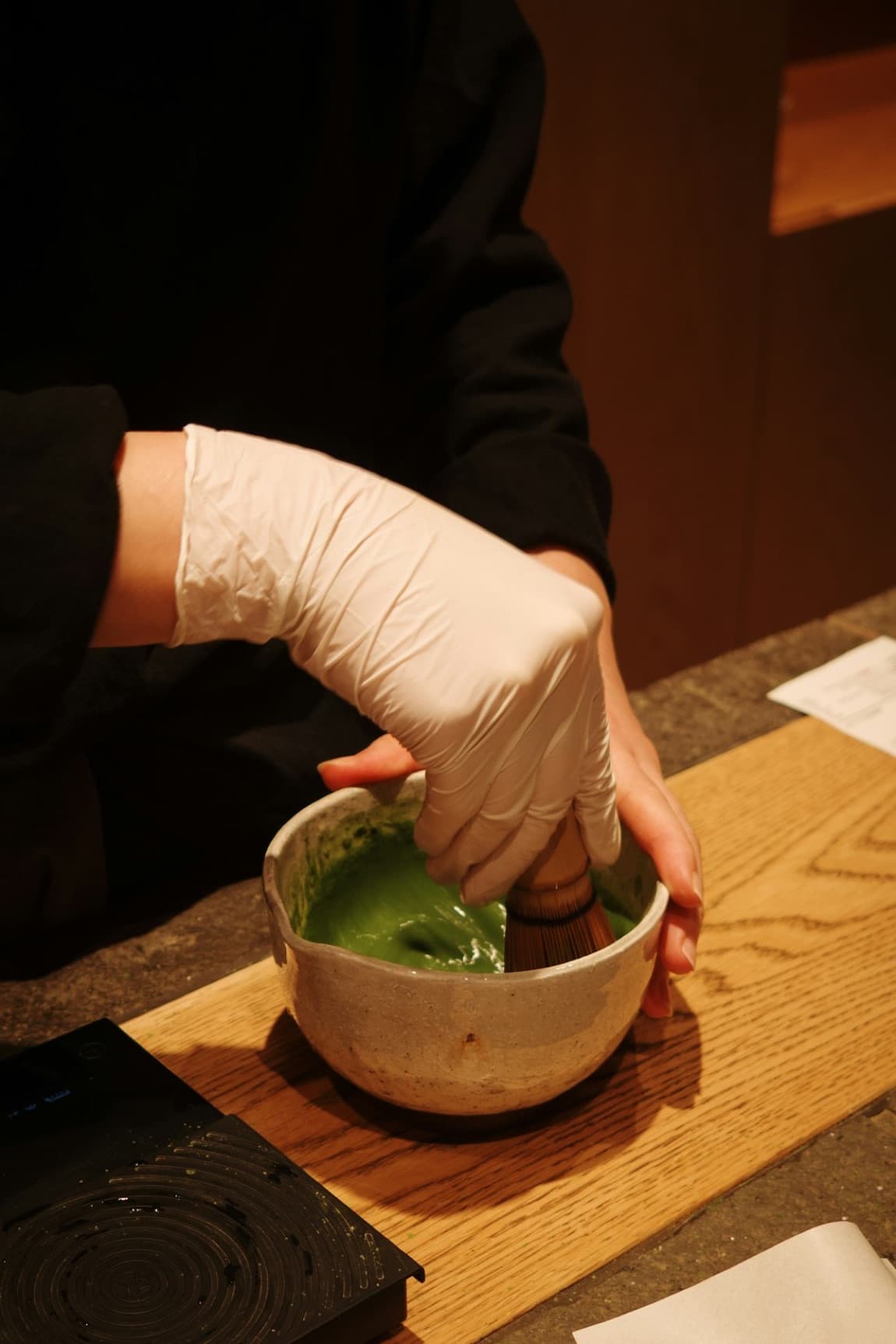 Una mano prepara il matcha in una ciotola di ceramica con il frustino di bambù, il verde brillante del tè