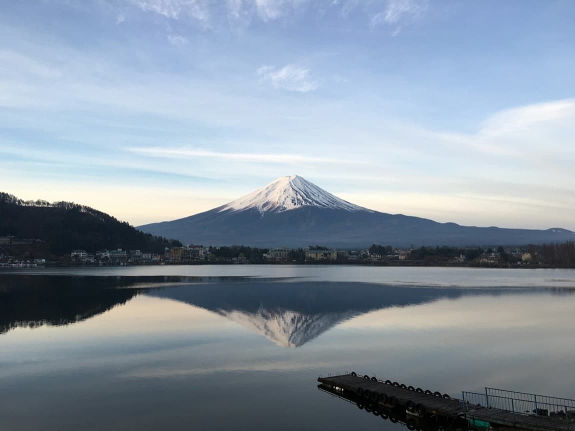 Il Monte Fuji innevato che si specchia in un lago calmo all'alba, con i monti scuri intorno