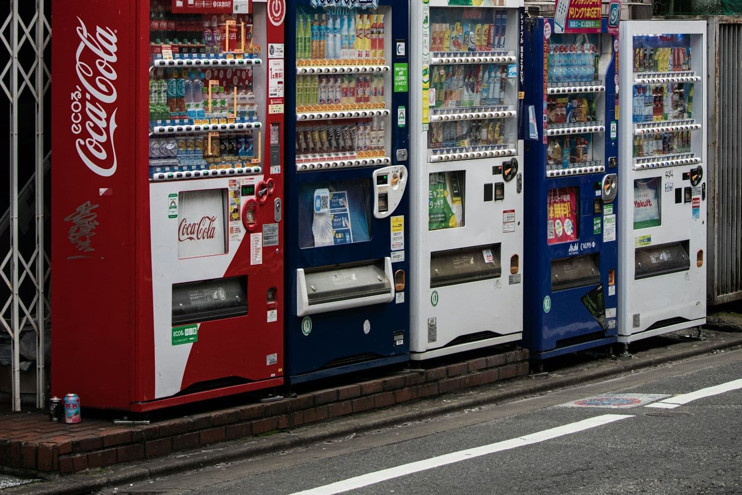 Una fila di distributori automatici di bevande lungo una strada giapponese, con i prezzi in yen esposti