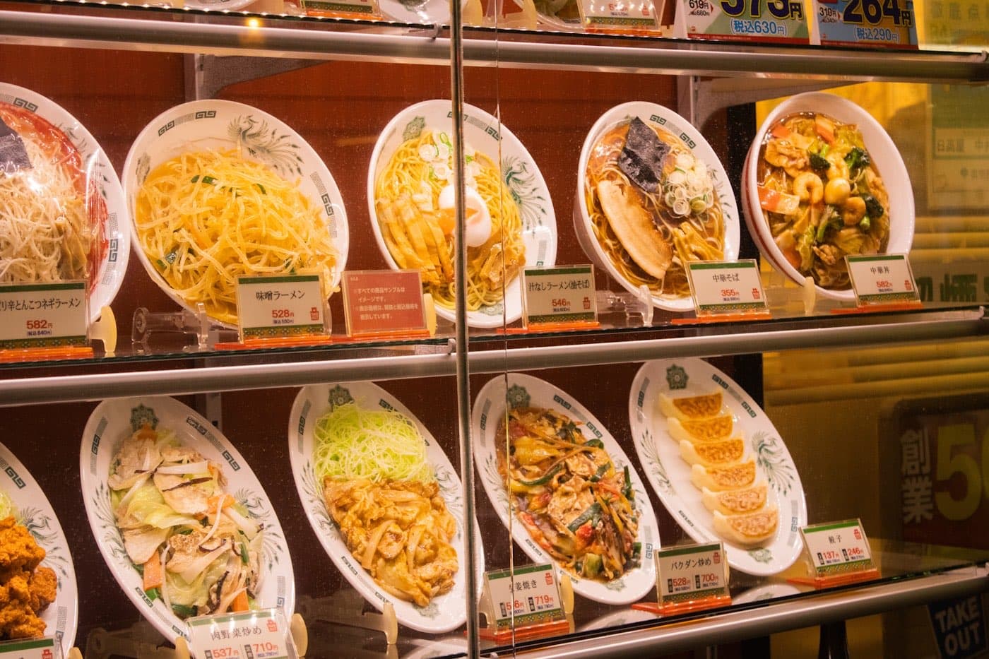 Una vetrina giapponese con modelli di plastica di ramen e altri piatti, ciascuno con il cartellino del prezzo