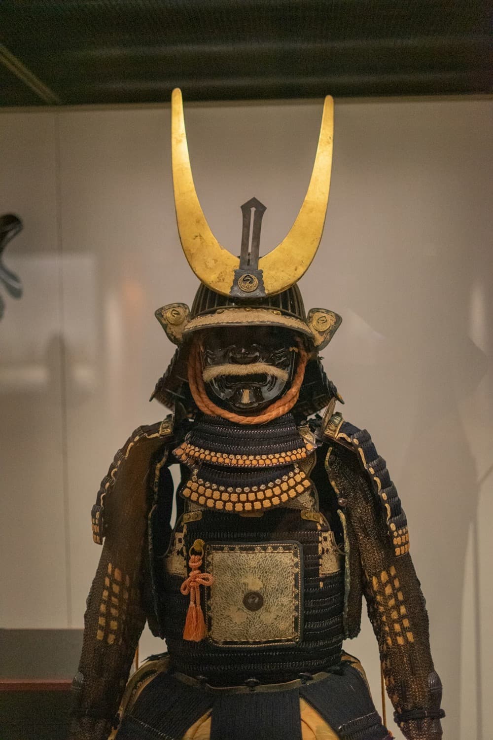Un'armatura di samurai esposta in un museo, con l'elmo dalle grandi corna dorate e la maschera scura