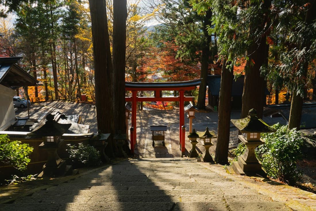 Un torii rosso in cima a una scalinata di pietra, tra gli aceri rossi d'autunno e le lanterne