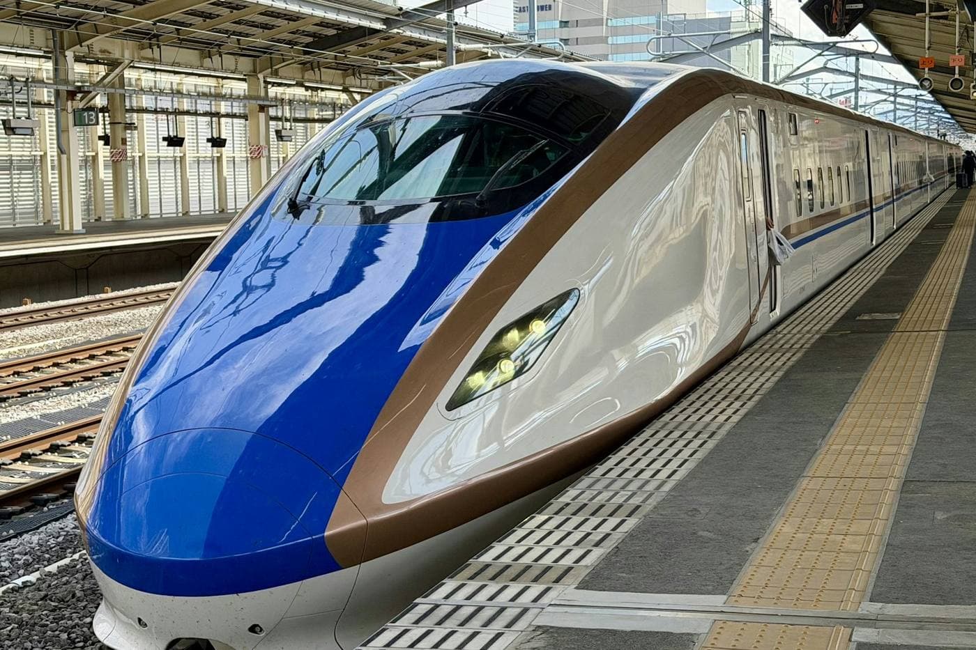 Il muso affusolato di uno shinkansen bianco, blu e rame fermo al binario di una stazione giapponese