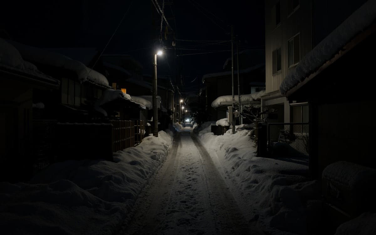 Una stradina residenziale giapponese deserta di notte, con la neve ai lati