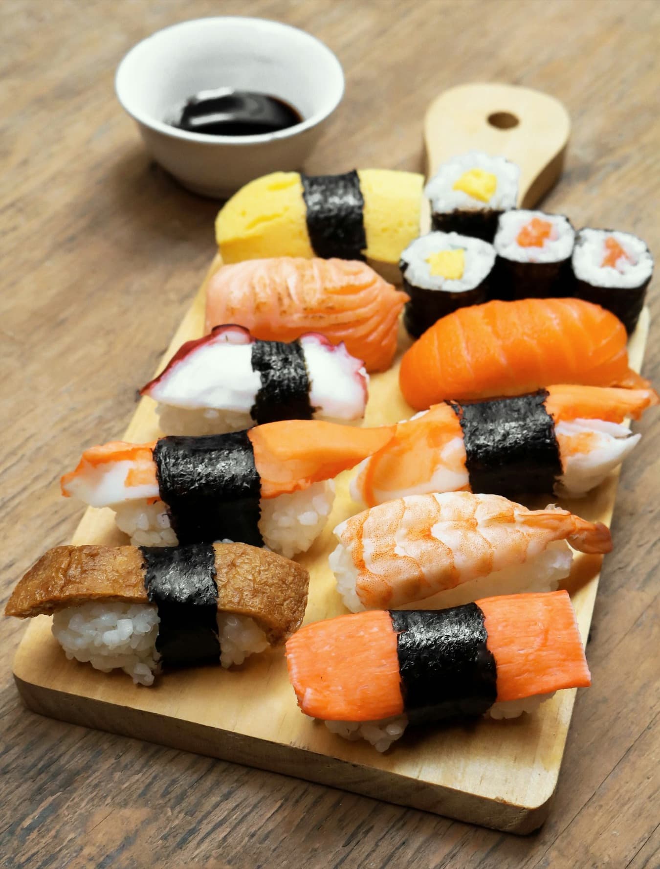 Un tagliere di nigiri sushi assortiti, con salmone, gambero e tamago, e una ciotolina di salsa di soia