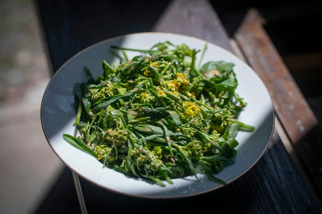 Un piatto bianco di verdure di primavera con piccoli fiori gialli, condite in modo semplice