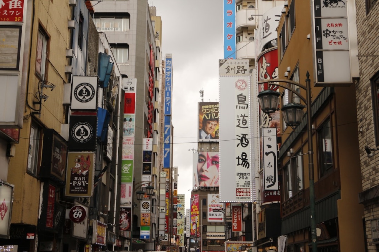 Una via di Shinjuku fitta di insegne verticali in giapponese, con manifesti pubblicitari sui palazzi