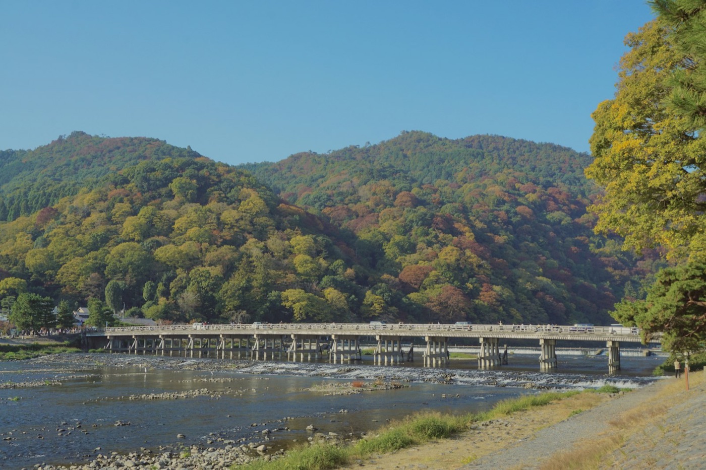 Il ponte Togetsukyo di Arashiyama sul fiume, con le montagne verdi e i primi colori dell'autunno alle spalle