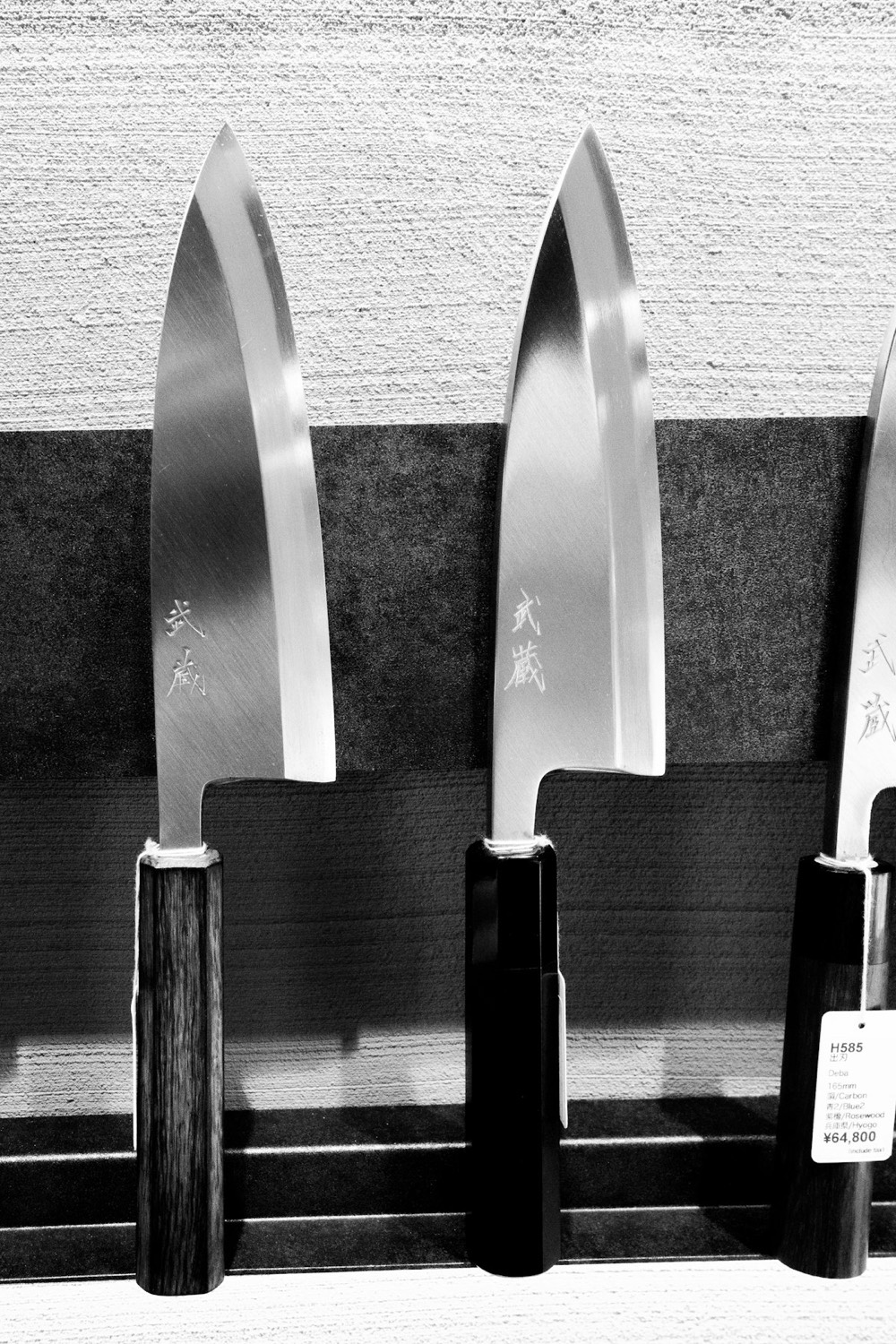 Due raffinati coltelli da cucina giapponesi con la lama lucida firmata dal maestro e il manico di legno, esposti in negozio