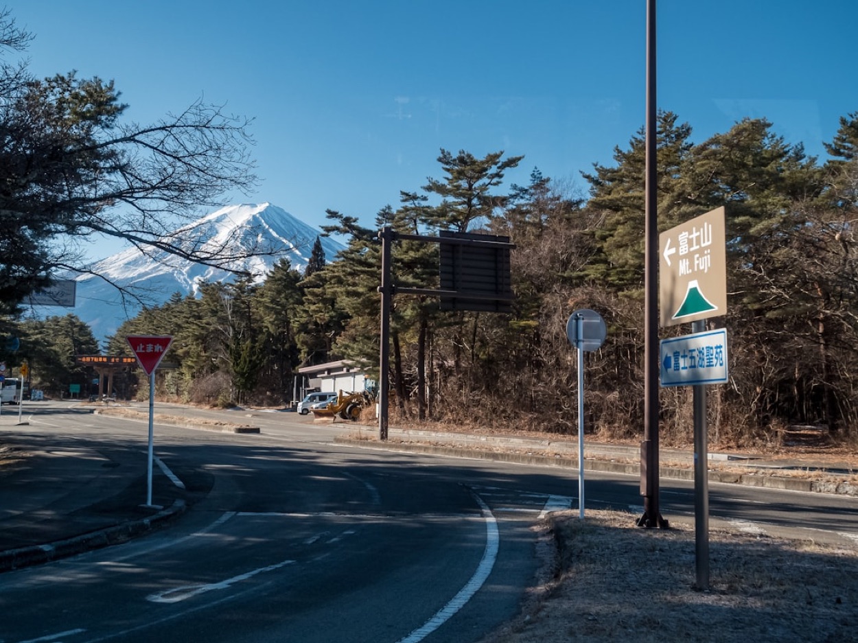 Una strada giapponese con i cartelli stradali in giapponese che indicano il monte Fuji, innevato sullo sfondo sotto un cielo azzurro