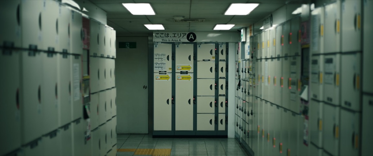 Una fila di coin locker bianchi in una stazione giapponese, con le indicazioni "Area A" in giapponese