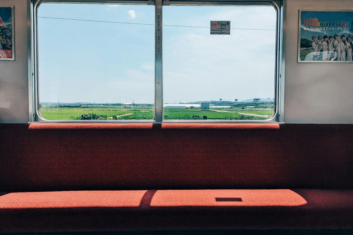 L'interno di un treno locale giapponese con i sedili rossi e la campagna che scorre fuori dal finestrino