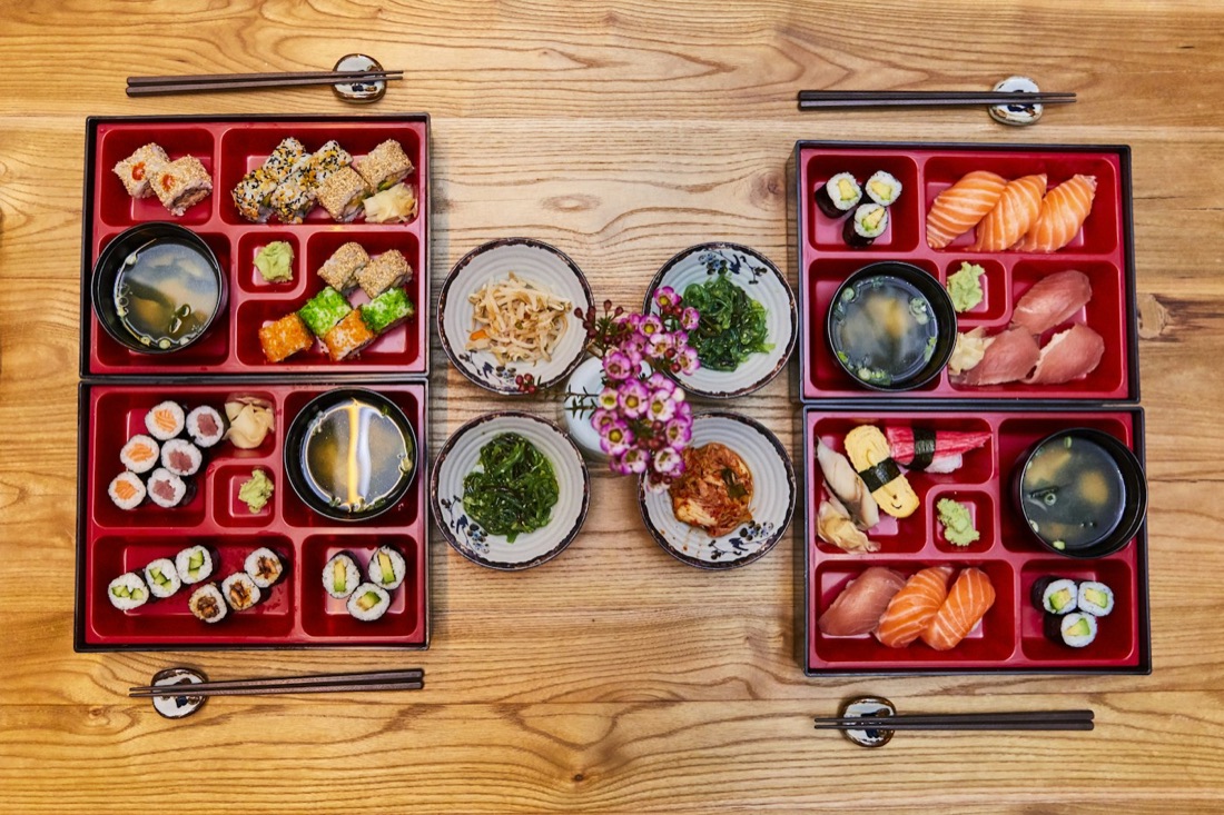 Quattro bento in scatole di lacca rossa viste dall'alto, con sushi, riso e contorni