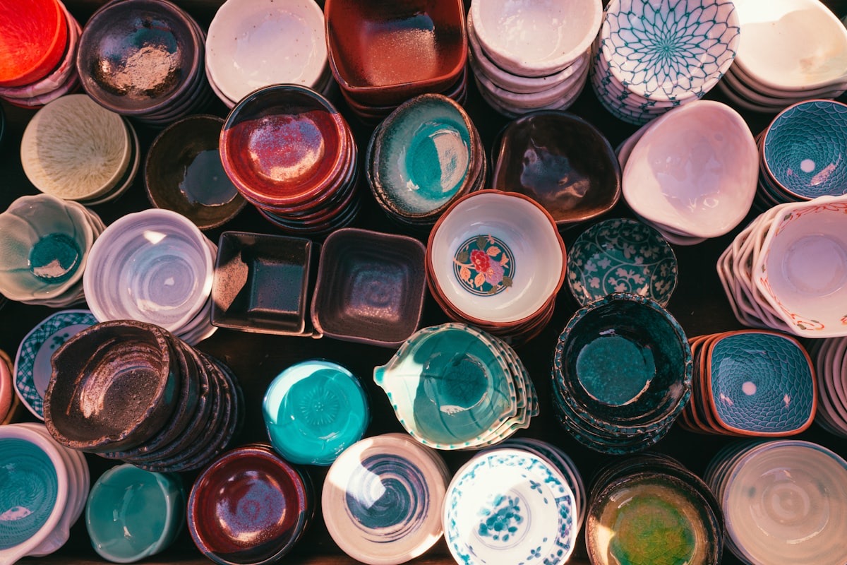 Molte ciotole e piattini di ceramica giapponese visti dall'alto, con smalti di colori diversi