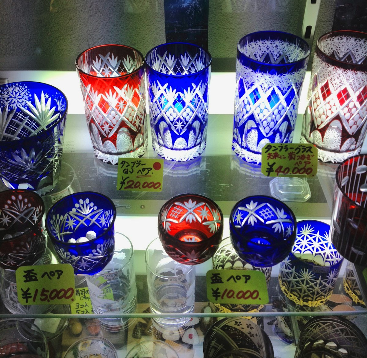Bicchieri di vetro tagliato Edo kiriko blu e rosso, con motivi geometrici finissimi, esposti in una vetrina illuminata