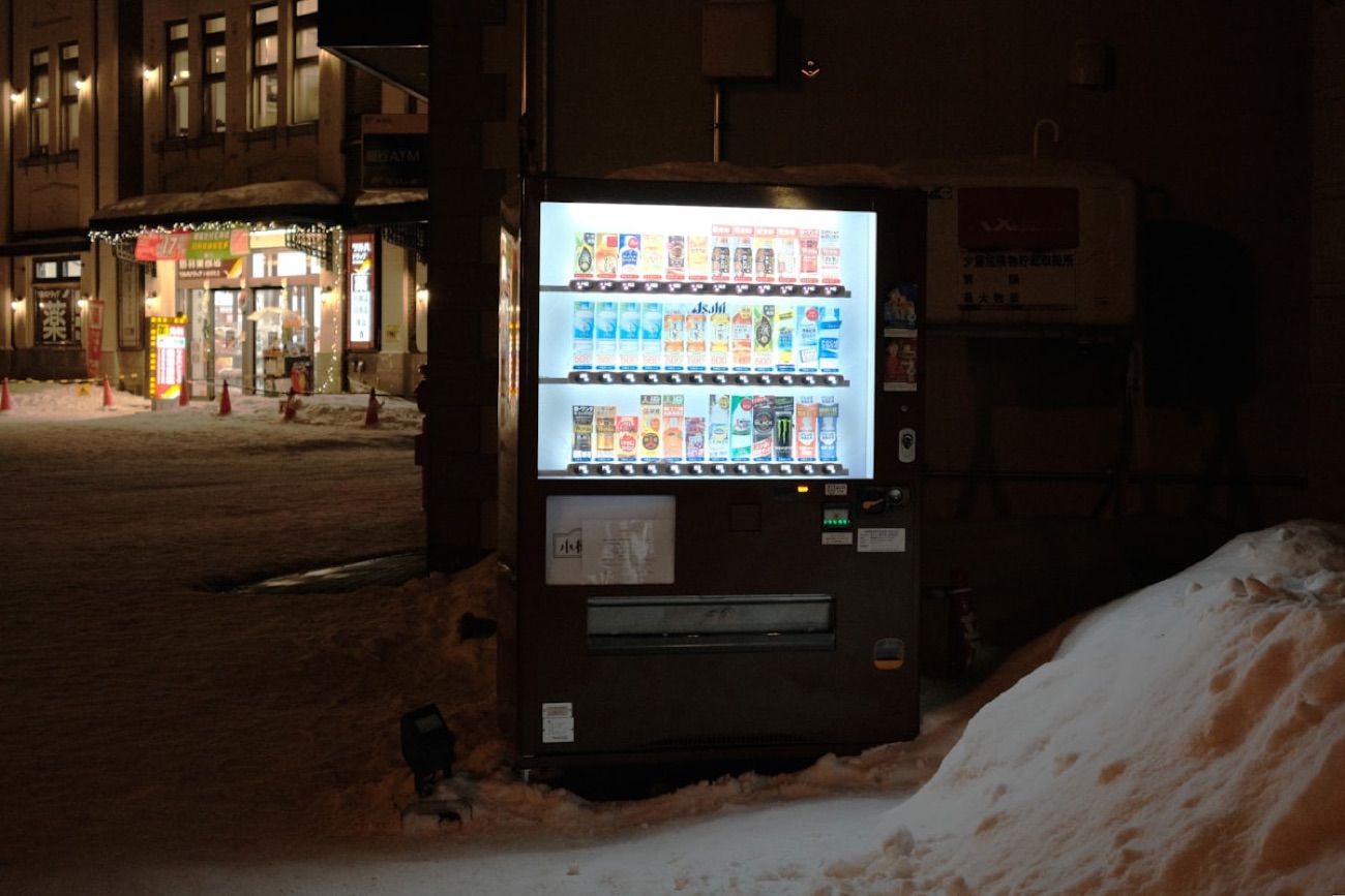 Un distributore automatico in mezzo alla neve in un paesaggio invernale giapponese, con le bevande calde in evidenza
