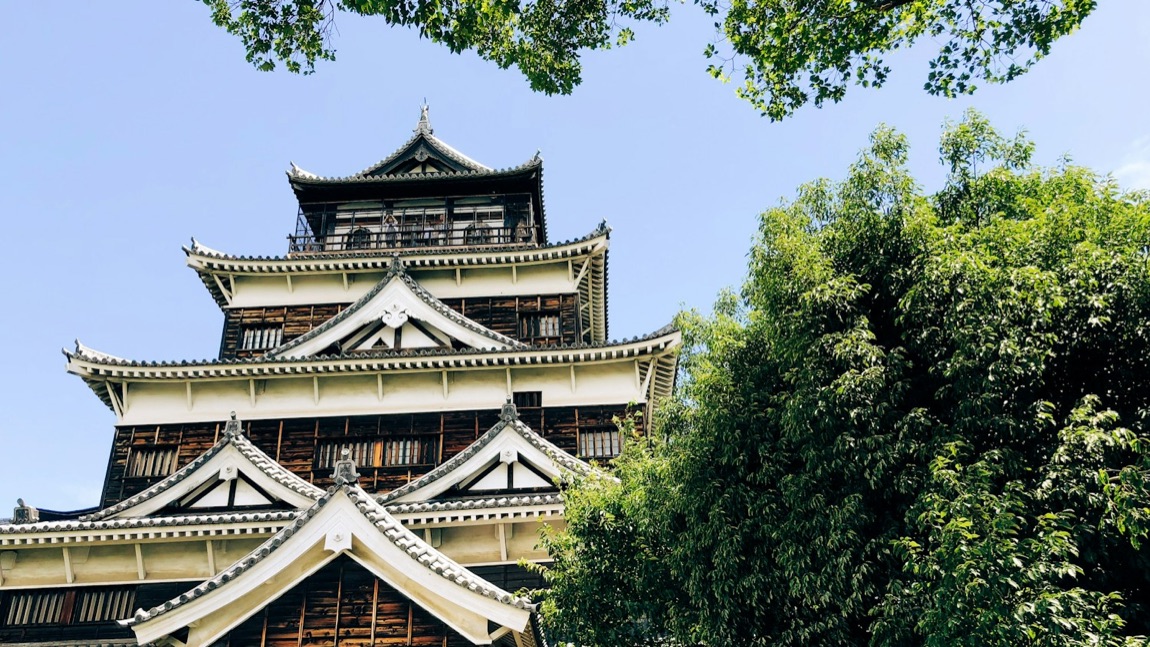 Il castello di Hiroshima in legno scuro e bianco sotto un cielo azzurro, tra il verde