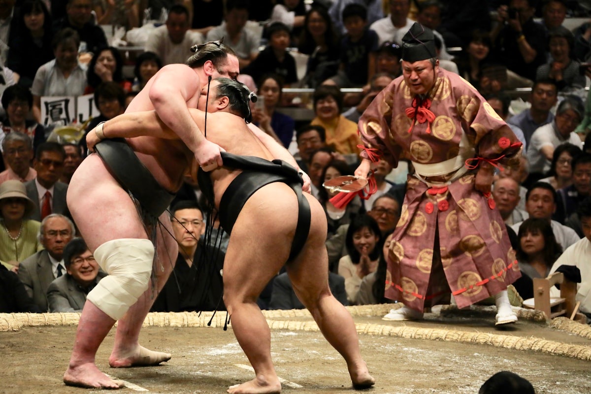 Due lottatori di sumo si affrontano sul ring davanti all'arbitro in kimono e al pubblico gremito