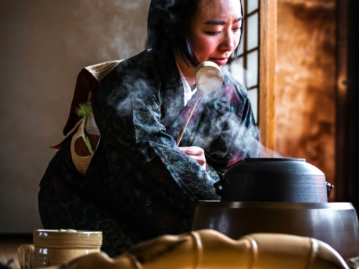 Una donna in kimono prepara il tè in una stanza con tatami, con il vapore che sale dalla caldaia