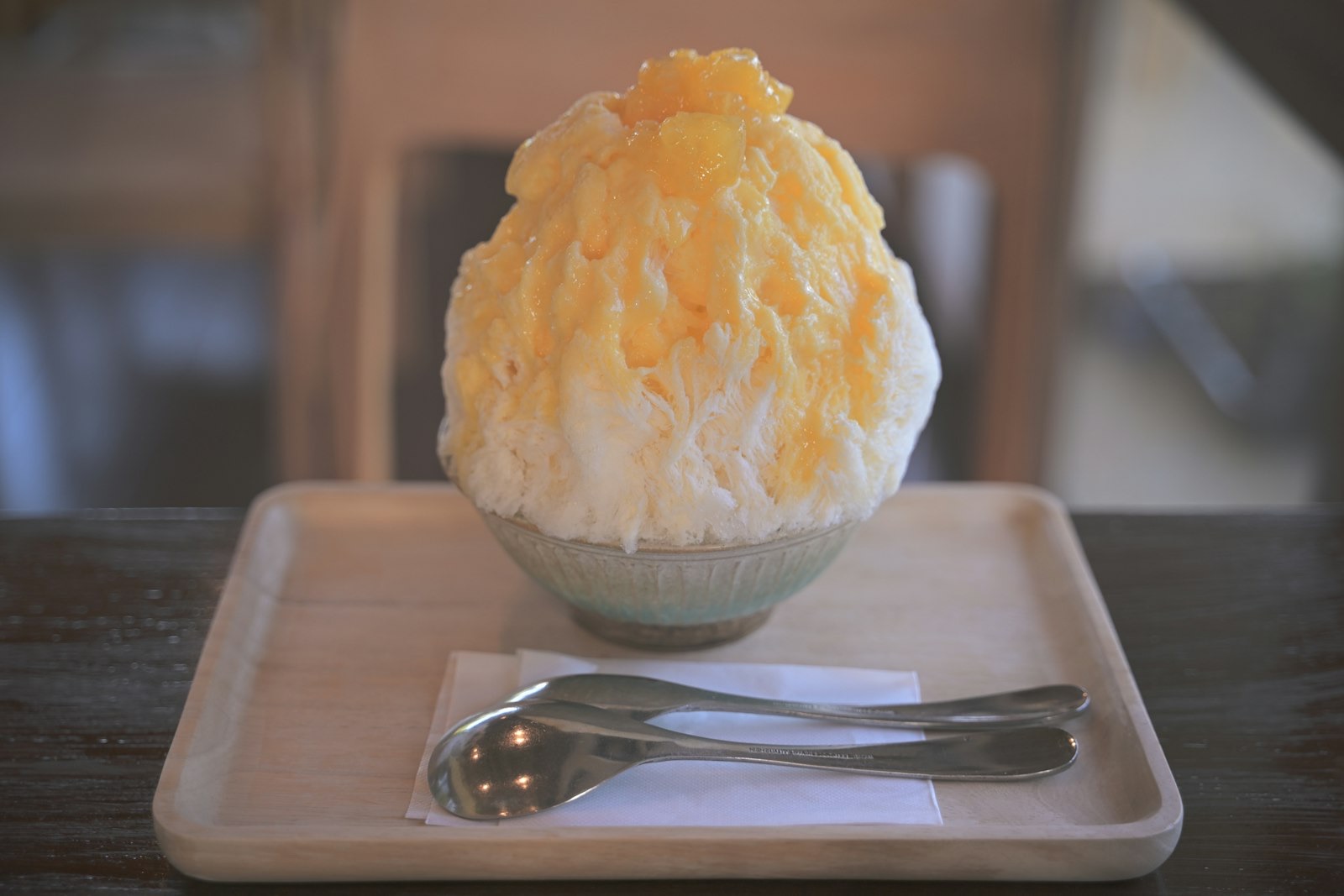 Una montagnetta di kakigori, ghiaccio tritato morbido come neve, con sciroppo di mango, servita in una coppetta su un vassoio di legno