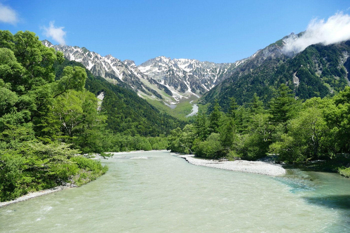 Le Alpi giapponesi d'estate a Kamikochi: un fiume turchese scorre in una valle verde sotto le cime ancora spolverate di neve