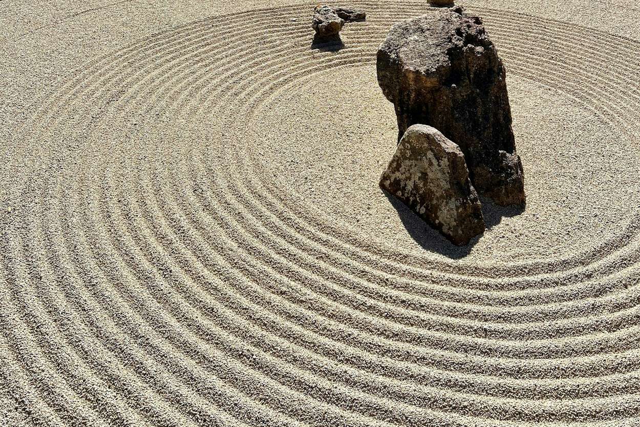 Un giardino secco giapponese con la ghiaia chiara rastrellata a cerchi concentrici intorno a un gruppo di pietre