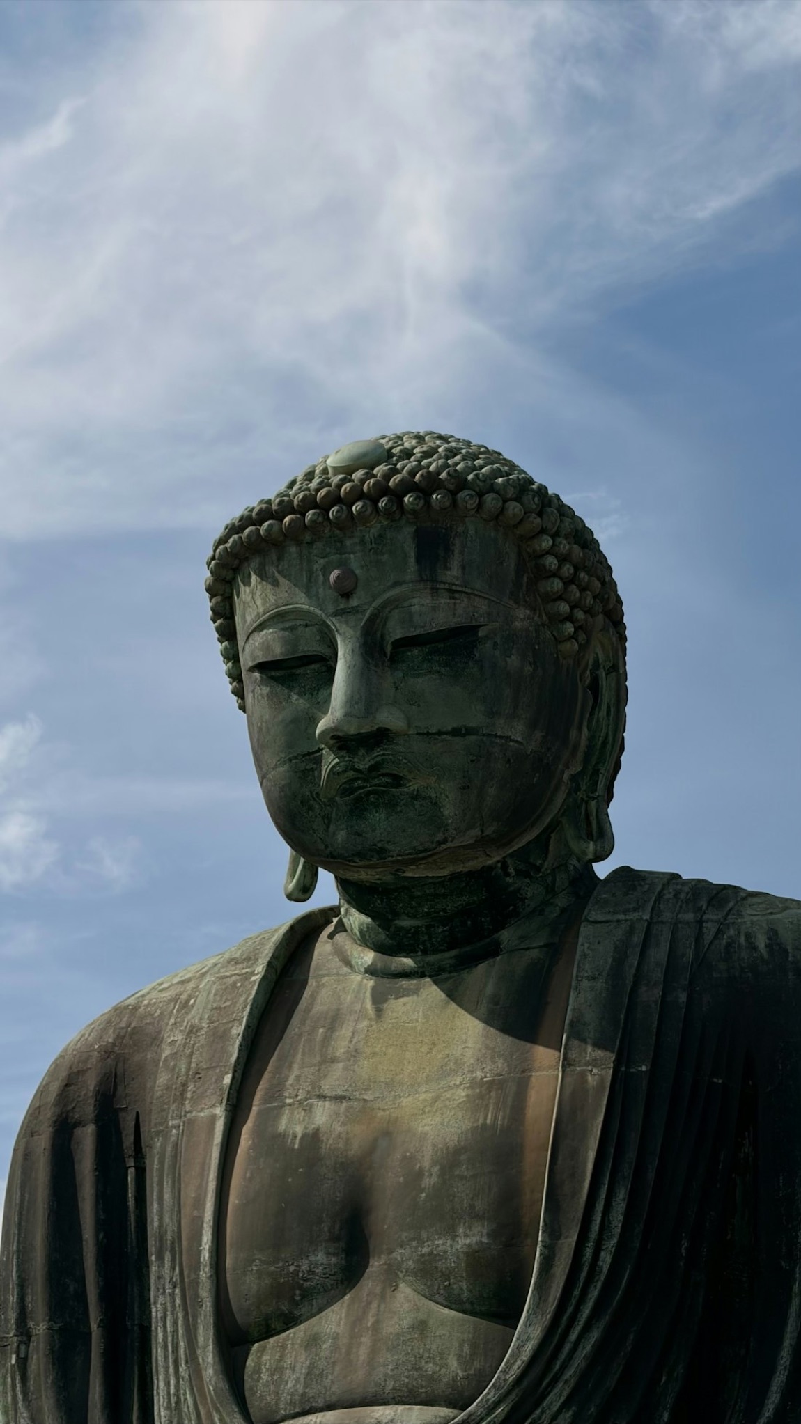 Il Grande Buddha di bronzo di Kamakura, seduto in meditazione, contro un cielo azzurro