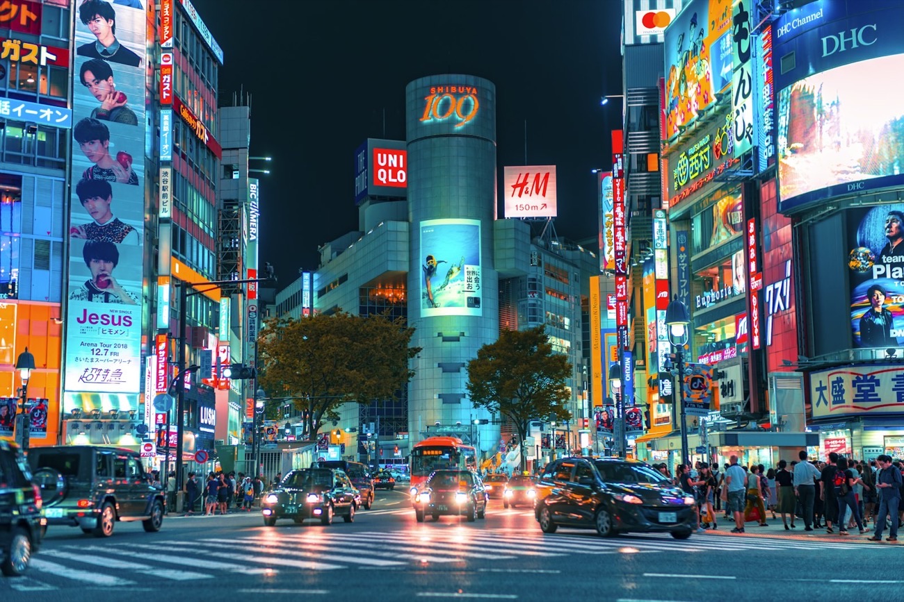 L'incrocio di Shibuya a Tokyo di notte, illuminato da mille insegne al neon, con le auto e la folla