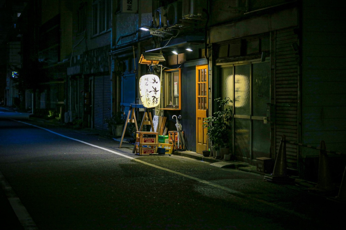Una lanterna di carta illuminata davanti a un piccolo locale, in una via silenziosa di notte