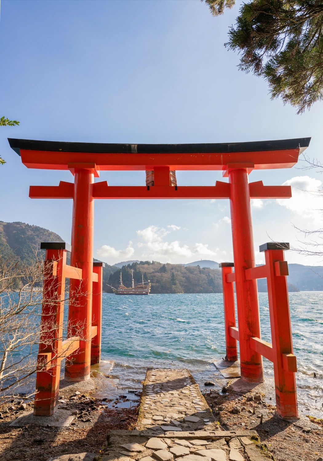 Il torii rosso del santuario di Hakone sul lago Ashi, con una nave turistica che passa sullo sfondo
