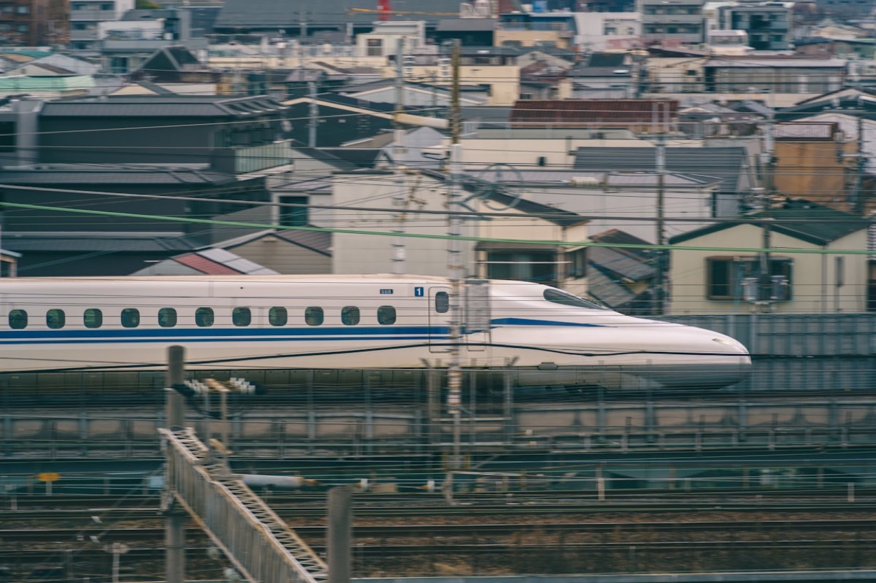 Uno shinkansen bianco e blu sfreccia sopra un quartiere residenziale giapponese